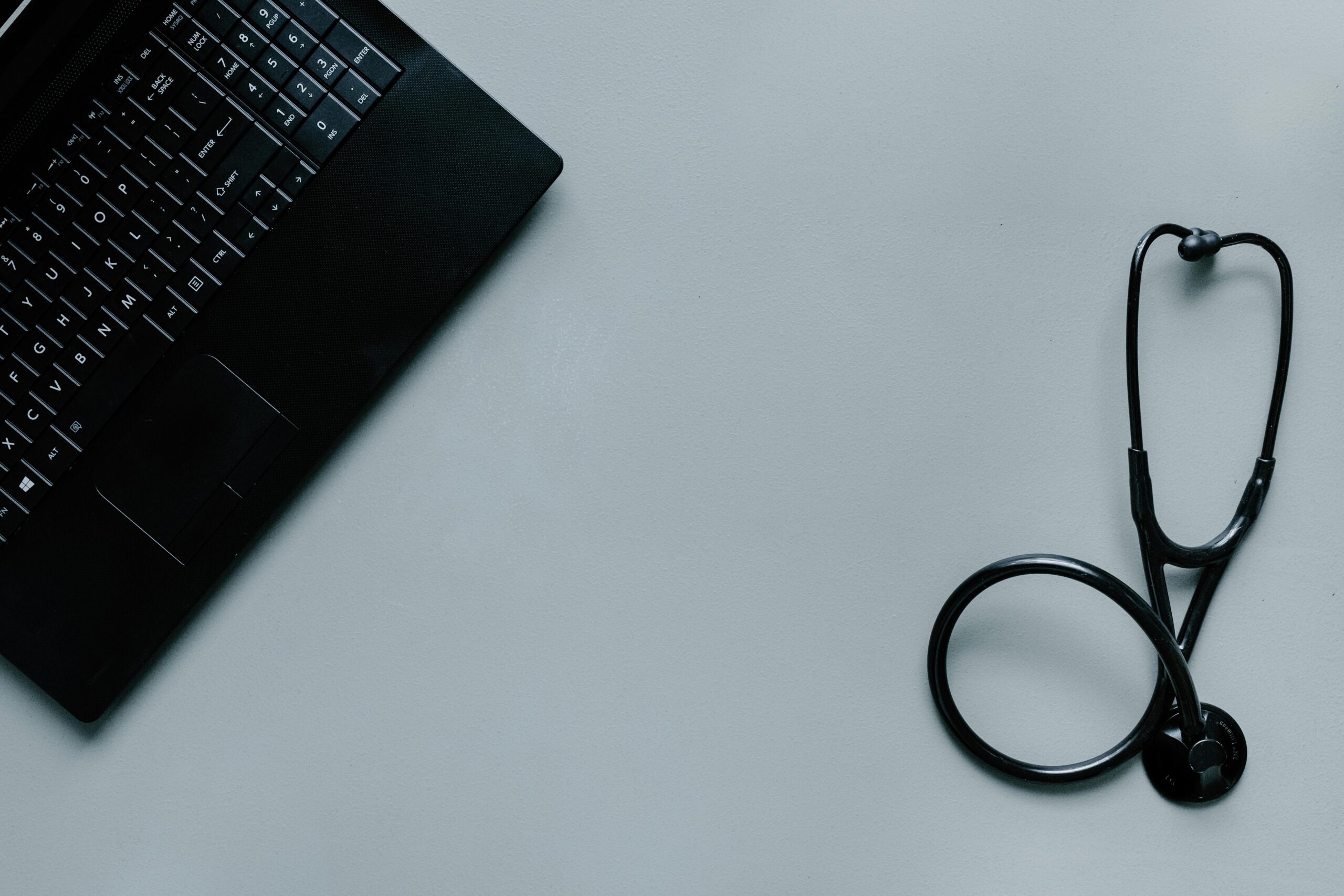 Minimalist image depicting a laptop and stethoscope representing telemedicine and digital health.